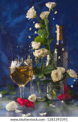 Valentines day.Splash of white wine. Romantic evening. Wine, a bunch of white roses and red hearts with smokeon a blue background. Holiday of lovers. A delicious alcoholic drink for two people.Picture