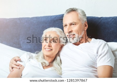 portrait of smiling senior couple wathcing tv at home sitting in the bed