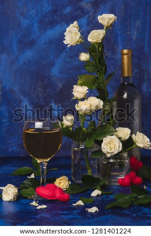 Valentine day. White wine. Romantic evening. A glass wine, a bunch of white roses and red hearts with smoke on a blue background. Holiday of lovers. A delicious alcoholic drink for two people.
