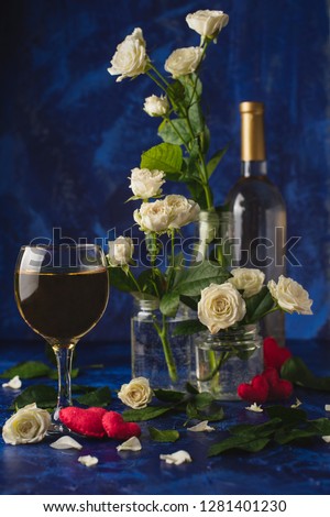 Valentine day. White wine. Romantic evening. A glass wine, a bunch of white roses and red hearts with smoke on a blue background. Holiday of lovers. A delicious alcoholic drink for two people.