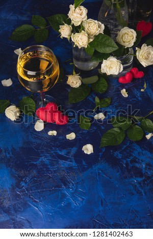 Valentine day. White wine. Romantic evening. A glass wine, a bunch of white roses and red hearts with smoke on a blue background. Holiday of lovers. A delicious alcoholic drink for two people.Top view