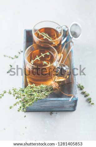 Transparent glass cup of herbal tea with thyme and sprigs of thyme tied in bunch in blue wooden box on white background