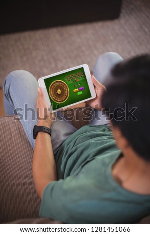 Online Roulette Game  against high angle view of man using digital tablet while sitting in living room