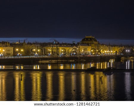 The night panorama view of famous Smetanovo Nabrezi street with Vltava river with reflection in the foreground captured from the Charles Bridge. Prague, Czech Republic