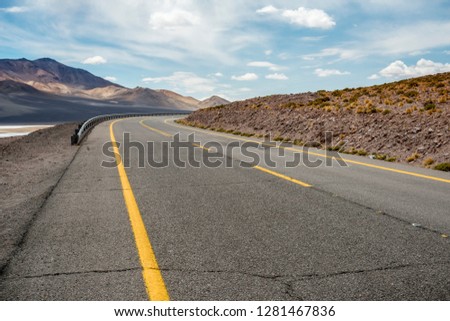 route that runs under the sunny mountains and the sky with clouds, you can see a crack in the asphalt