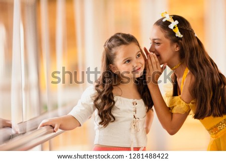 Girl whispering into sister's ear.
