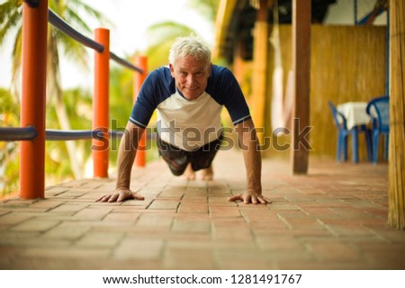 Mature man smiles as he does a press up on a balcony and poses for a portrait.