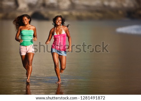 Two girls running along beach, El Salvador.