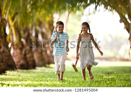 Brother and sister running together holding croquet mallets.