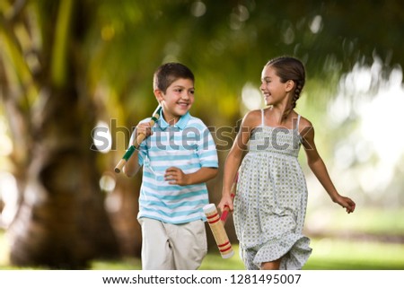Brother and sister running together holding croquet mallets.