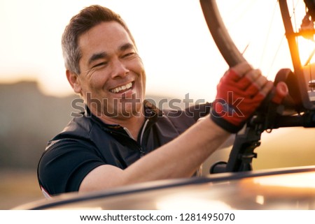 Mature man lifting his bike off a car