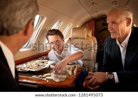A boy playing dominos with businessmen on an airplane