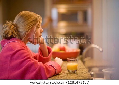 Girl sitting at kitchen counter with glass of orange juice in the morning