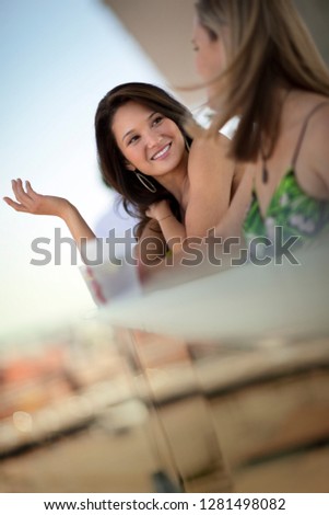 Two smiling young women chatting on a balcony.