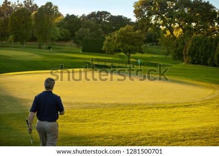 Middle aged man walking toward a flag on a golf course.