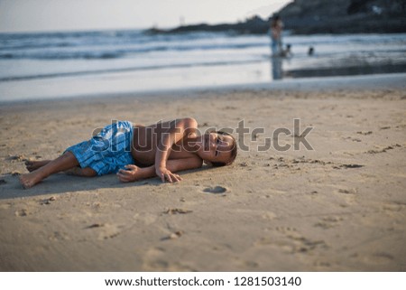 Young boy lying on the beach looking happy