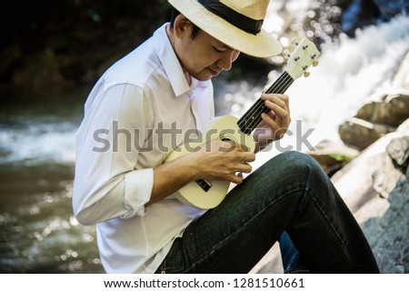 Man play ukulele near to the waterfall - people and music instrument life style in nature concept 