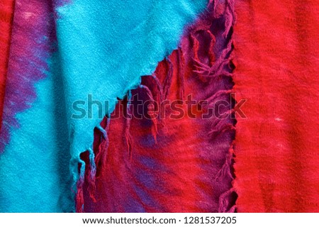 Close up of multi colored tie dyed fabric background showing tassels in shades of blue, red, purple.