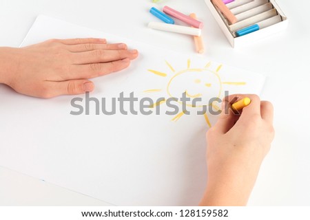Child's hand drawing a pastel crayon smiling sun