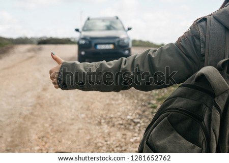 Close-up of a tourist girl with a backpack hitch-hiking. She raised her finger up and tried to stop the car to continue her journey.