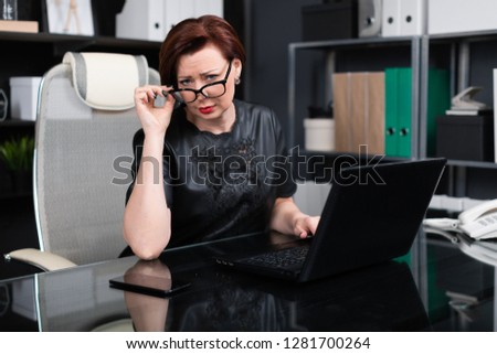 Stylish woman lifted her glasses and looks right sitting at table in office
