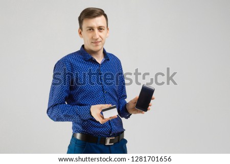 young man with a Bank card and mobile phone stands isolated on light background