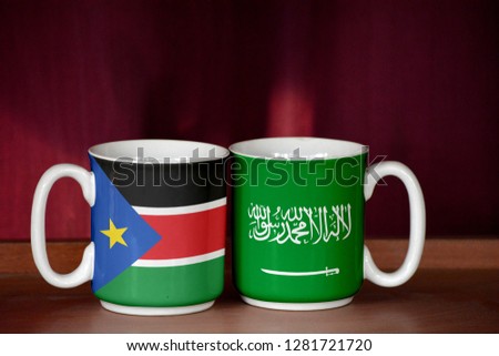 Saudi Arabia and South Sudan flag on two cups with blurry background