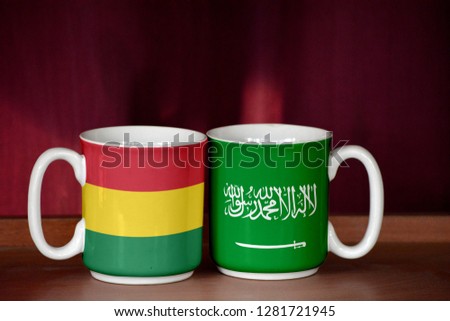 Saudi Arabia and Bolivia flag on two cups with blurry background