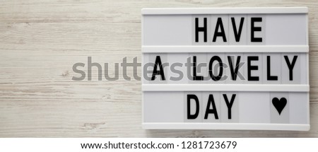 Lightbox with text 'Have a lovely day' on a white wooden surface, top view. From above, flat lay, overhead. Copy space.