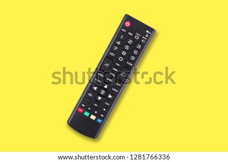 Single black plastic remote control for different multimedia devices in center on yellow background. Top view
