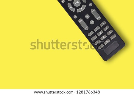 Single black plastic remote control for different multimedia devices on yellow background with copy space for your text. Top view