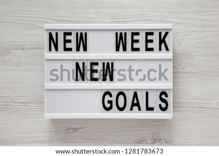 Modern board with text 'New week new goals' over white wooden surface, top view. From above, flat lay, overhead. 