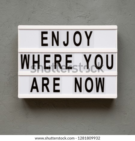 'Enjoy where you are now' words on lightbox over concrete background, top view. Flat lay, from above, overhead.
