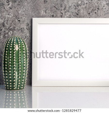 White empty mockup frame on a stone wall background. Place for text. Ceramic cacti as decoration. White smooth shelf. Front view, real photo