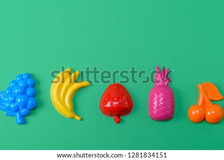 multicolored plastic toys fruits on a green background, copy space