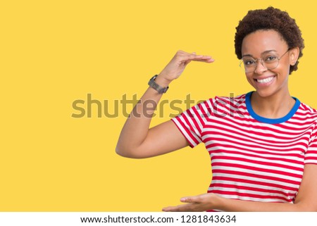 Beautiful young african american woman wearing glasses over isolated background gesturing with hands showing big and large size sign, measure symbol. Smiling looking at the camera. Measuring concept.