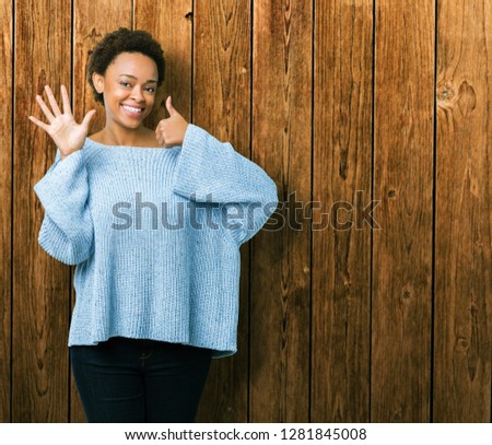 Young beautiful african american woman wearing a sweater over isolated background showing and pointing up with fingers number six while smiling confident and happy.