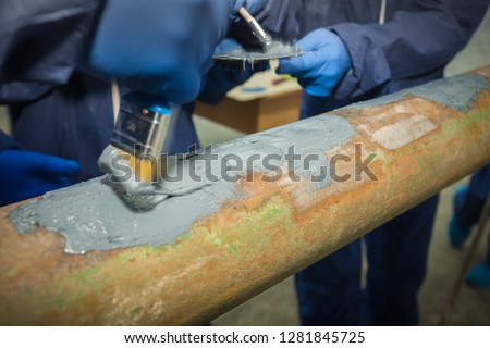 Restoration of the strength characteristics of the industrial pipeline. Resin coating on pipe. Hands and spatulas. Picture taken in Ukraine, Kiev region. Color image