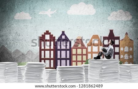 Thoughtful businessman looking away while sitting on pile of documents with drawn cityscape on background. Mixed media.