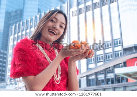 Chinese new year, Beautiful Asian Chinese girl in Qipao traditional dress holding lucky orange against modern buildings in the city.