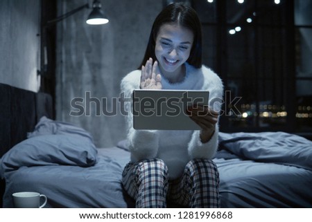 Photo of young woman sitting on bed with tablet communicating via video chat