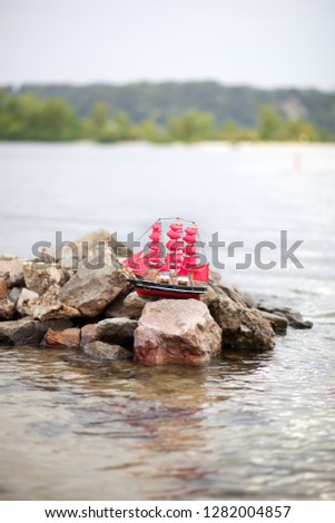Scarlet Sails. A lone ship against morning sky. Ship in water. Alexander Green. Photography for Alexander Green's novel. Ship with scarlet sails in the river. Wooden figurine of a ship with red sails 