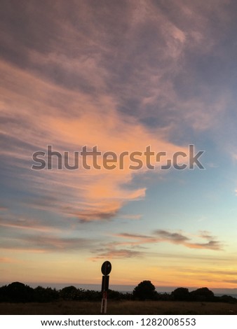 Wonderful romantic landscape view over a colorful sunset, with pink, orange, yellow and blue colors, clouds, road sign & threes in the horizon, giving emotions, peaceful, magic and relaxing feeling.
