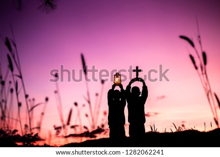 Two children holding oil lamp and christian cross with light sunset background,christian concept.