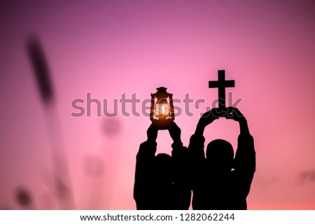 Two children holding oil lamp and cross with light sunset background,christian concept.