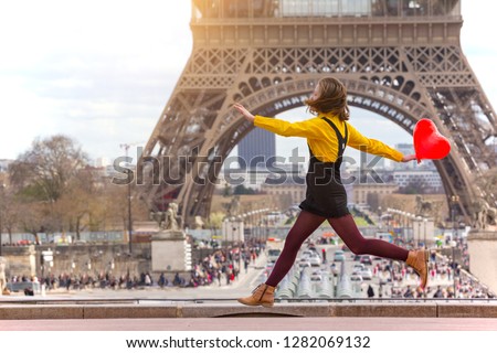 happy and smiling girl student with a balloon in the shape of a hearton jumps the background of the Eiffel Tower in Paris. France 
