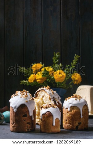 Set of traditional Russian and Ukrainian Easter cake Kulich Paska bread glazed with almond, whole and sliced, with yellow flowers, colored eggs, cottage paskha over dark texture table. Rustic style
