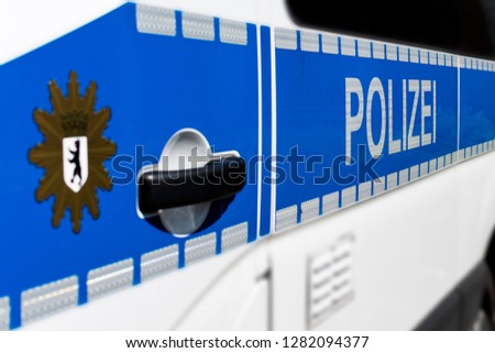Side detail view of a Berlin police car with the word "Polizei" and the blurred Berlin city coat of arms in the foreground