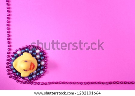 Yellow rubber duck and beads on a pink background