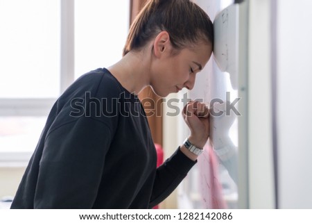 Young female student standing and writing on white chalkboard in a classroom